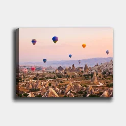 Lerretsbilde 70x100 cm - Flere fargerike varmluftsballonger svever over et dramatisk landskap med unike fjellformasjoner